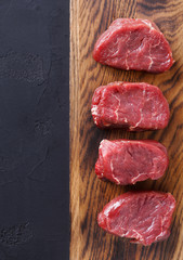 Raw beef filet mignon steaks on wooden board at blac