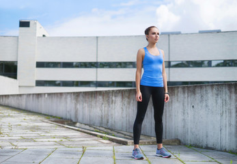Fototapeta na wymiar Young, fit and sporty woman standing in front of concrete cement wall. Fitness, sport, urban jogging and healthy lifestyle concept.