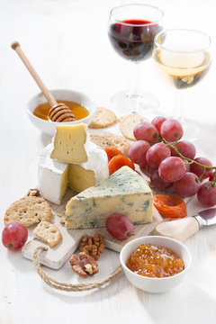 molded cheeses, fruit and snacks on a white wooden background, vertical