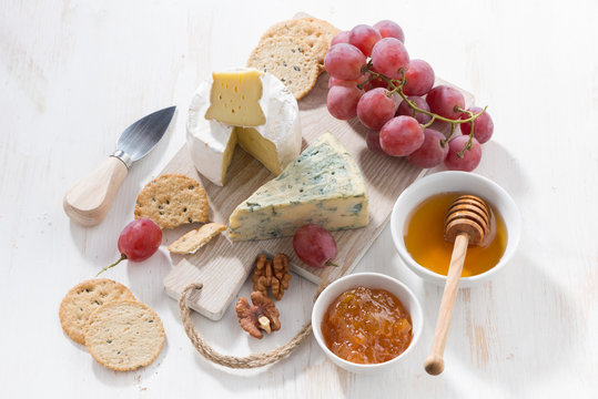 molded cheeses, fruit and snacks on a white wooden board, top view