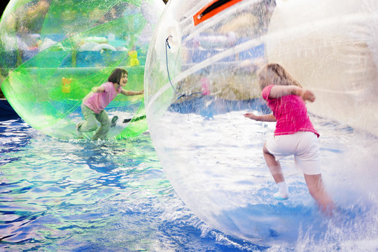 Two young girls playing inside a floating water walking ball.