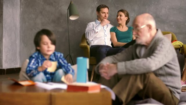 Grandfather and grandson play on floor in room on background parents on couch