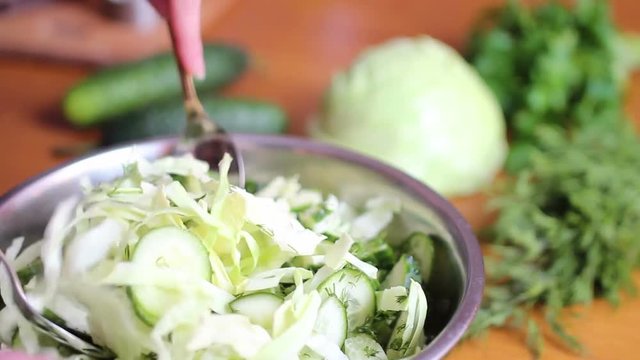 The cook mixes the freshly cut cucumbers in a metal bowl with green cabbage