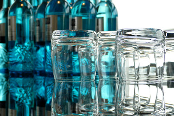 Glasses on a glass table with bottles of water in background