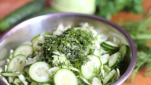 Cook with fresh salad salt sliced cucumbers in a metal bowl with green cabbage