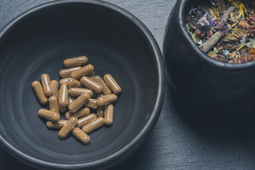 Herbal capsules in black ceramic bowl on stone background