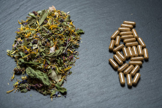 Herbal capsules and herbs on black stone background