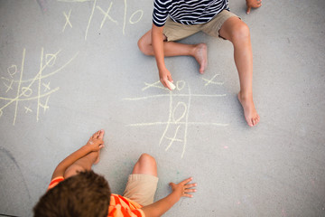 Two small boys chalking game of tic tac toe on driveway 