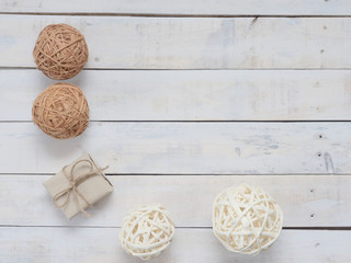 A present or gift box wrapped by rough brown recycled paper and tied with brown hemp rope as ribbon with white, brown, and black wicker wooden balls on white rough wooden background with green concept