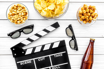 Crisp, popcorn, rusks for watching film. Clapperboard and glasses on white wooden background top...