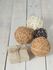 A present or gift box wrapped by rough brown recycled paper and tied with brown hemp rope as ribbon with white, brown, and black wicker wooden balls on white rough wooden background with green concept