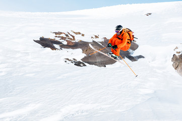 An athlete skier is jumping from high rock high in the mountains.
