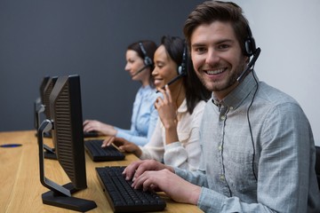 Business executives with headsets using computers at desk