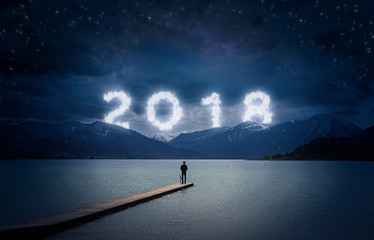 New year background, young man standing on a jetty in a lake and looking to the mountains under the...