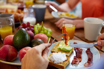 hands with bacon on fork at table full of food