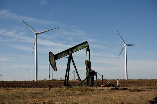 Low angle view of a crude oil pump jack framed by wind power turbines, new versus old technology in Texas, USA