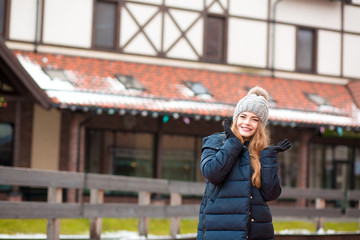 Stylish young woman in knitted hat and coat posing near the house. Space for text