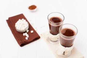 Warm cocoa in glasses with marshmallow, crocahet decorations, brown and beige napkins on white wooden background. Hot chocolate. Sweet drink. Close up photography. Hoizontal banner