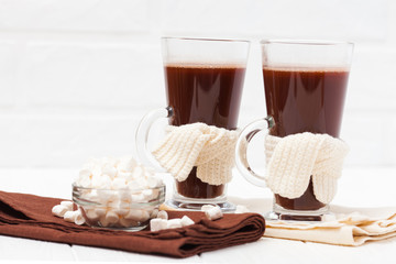 Warm cocoa in glasses with marshmallow, crocahet decorations, brown and beige napkins on white wooden background. Hot chocolate. Sweet drink. Close up photography. Hoizontal banner