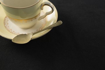 Empty cup with saucer and spoon on black background