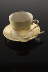 Empty cup with saucer and spoon on black background