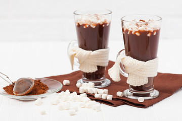 Warm cocoa in glasses with marshmallow, crocahet decorations, brown and beige napkins on white wooden background. Hot chocolate. Sweet drink. Close up photography. Hoizontal banner