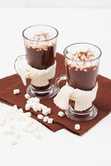 Warm cocoa in glasses with marshmallow, crocahet decorations, brown and beige napkins on white wooden background. Hot chocolate. Sweet drink. Close up photography. Vertical banner