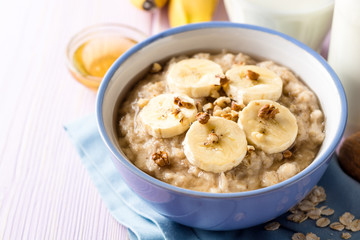 Oatmeal porridge with banana, walnuts and honey in bowl on purple wooden background. Healthy breakfast.