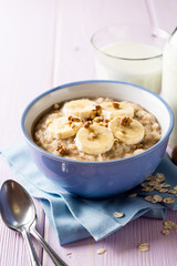 Oatmeal porridge with banana, walnuts and honey in bowl on purple wooden background. Healthy breakfast.