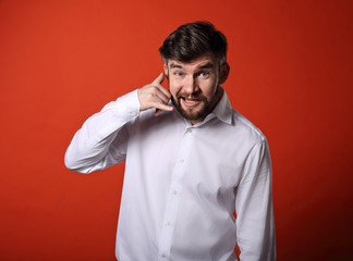 Smiling excited business man showing call me gesture on bright red background. Closeup portrait...