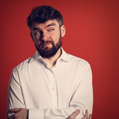 Thinking grimacing bearded fun man in whirt shirt looking on orange background with empty copy space. Closeup toned portrait