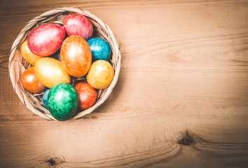 Multicolor Easter eggs in a basket on a wooden background.