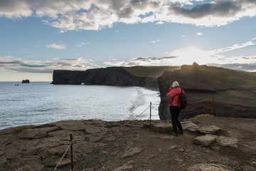 Fototapeta premium Woman stands on the top of cliff over the black beach
