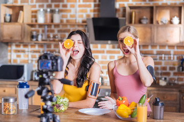 Fresh energy. Happy cute positive women holding orange halves and smiling while looking into the camera
