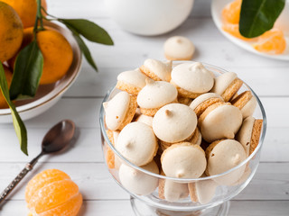 Cookies meringue in a glass vase mandarins with green leaves in a plate on white background