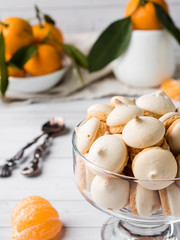 Cookies meringue in a glass vase mandarins with green leaves in a plate on white background
