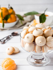 Cookies meringue in a glass vase mandarins with green leaves in a plate on white background
