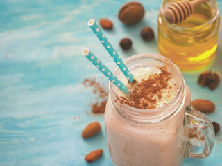 Banana smoothie decorated by cinnamon powder in mason jar on turquoise rustic wooden background with honey and nuts. Copy space