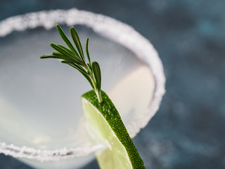 Glass of Martini coctail with fresh rosemary and lime on blue background.
