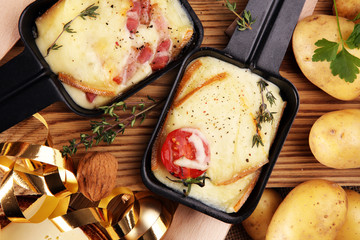 Delicious traditional Swiss melted raclette cheese on diced boiled or baked potato served in...