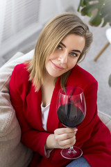 Attractive woman with a glass of red wine. Sits on the couch in her apartment