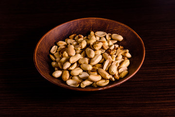 Peeled roasted peanuts in ceramic dish on wooden table