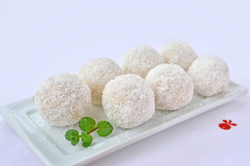Coconut white chocolate balls on white serving plate. Fancy confection truffles covered with desiccated coconut.