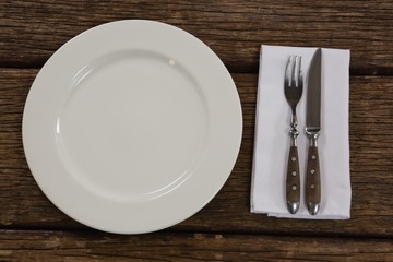 Plate with cutlery and napkin on wooden table