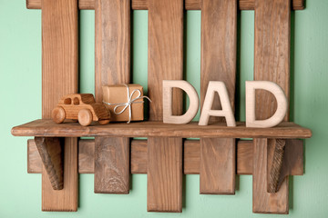 Word "Dad" made of wooden letters and gift box for Father's day on shelf