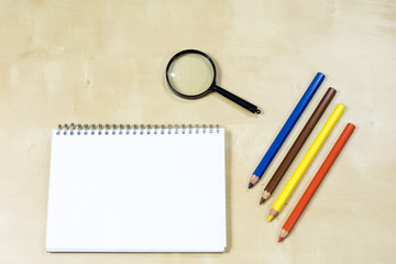 Pencils in a container and magnifier on a wooden table. Drawing accessories in a paper cup on a wooden drawing table and a magnifying glass.