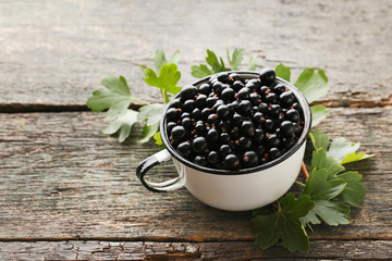 Black currants in mug with leafs on grey wooden table