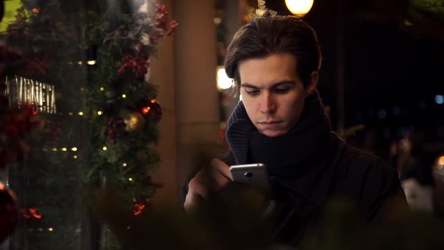 Portrait of young man using smartphone on a busy city street in evening