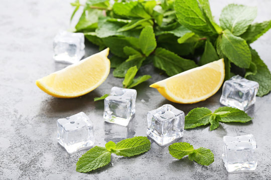 Mint leafs with lemons and ice cubes on grey wooden table