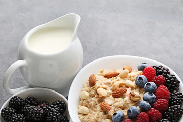 Oatmeal in bowl with berries and jar of milk on wooden table